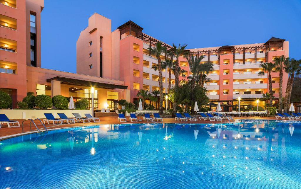 Luksusa viesnīca ar baseinu, apzaļumotu apkārtni un modernu arhitektūru. Vakarā apgaismota, radot relaksējošu atmosfēru.