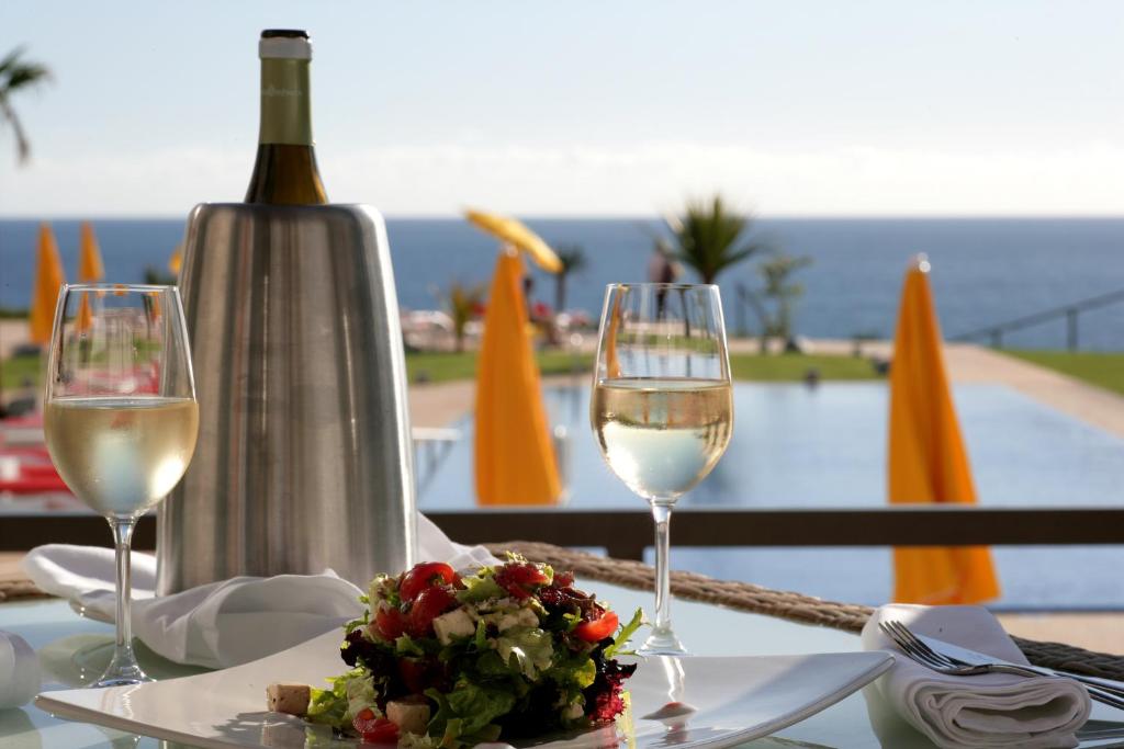 Elegants galda iestatījums ar baltvīnu un svaigu salātu šķīvi, skats uz jūru un baseinu. Ideāla atmosfēra relaksācijai un izsmalcinātai ēšanai.
