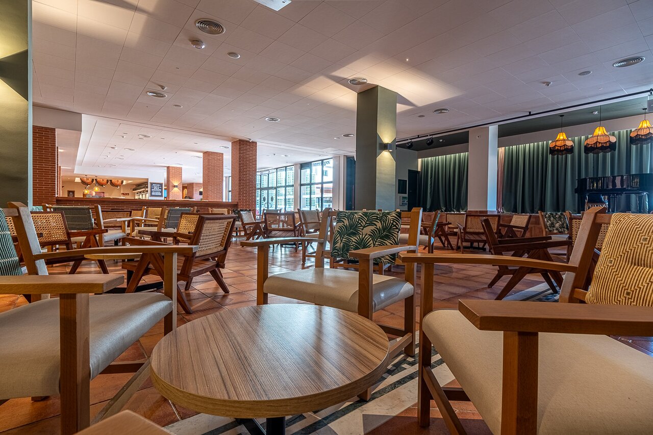 Estival Park Marena plašā atpūtas zona ar ērtiem koka krēsliem un klavierēm fonā.