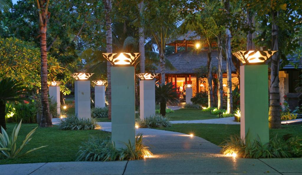 Dārza ceļš, apgaismots ar stilīgām laternām, ved uz māju, ko ieskauj zaļumi un koki. Pielāgota ainava rada mierīgu un relaksējošu atmosfēru.