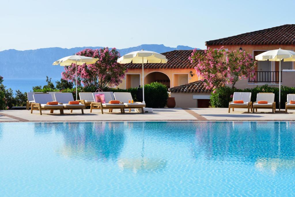 Luksusa viesnīcas baseins ar sauļošanās krēsliem un saulessargiem, apstādījumiem un kalnu ainavu fonā. Ideāla vieta atpūtai un relaksācijai.