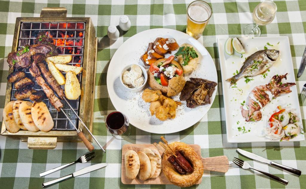 Bagātīgs gaļas grilēšanas ēdiens, kas ietver šašlikus, ceptus kartupeļus, zivi un garneles, pasniegts ar salātiem un maizi. Uz galda ir arī dzērieni un dekoratīvi elementi.