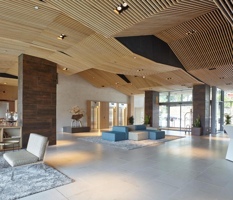 Mūsdienīga viesnīcas recepcija ar elegantu koka griestu dizainu un plašu, gaišu telpu, kurā redzami dīvāni un eleganti aksesuāri.