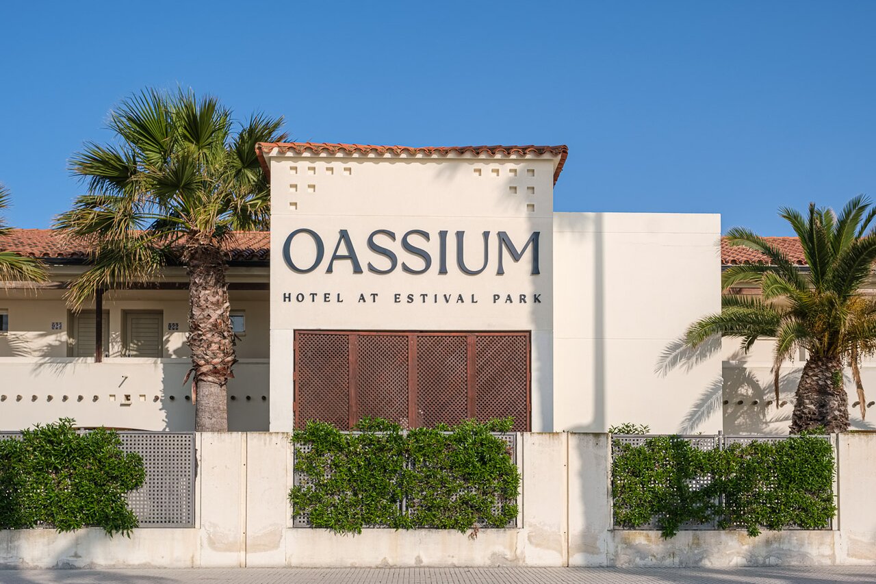 Oassium Hotel - Adults Only fasāde ar palmām un izkārtni saulainā dienā.