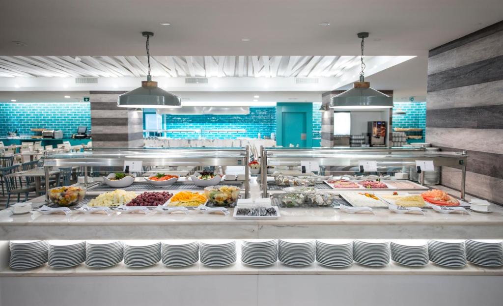 Šis ir moderns bufetes galds ar dažādām svaigām dārzeņu un augļu izvēlēm, kā arī gaļas un jūras velšu ēdieniem, kas atrodas viesnīcas restorānā ar gaišu un stilīgu interjeru.