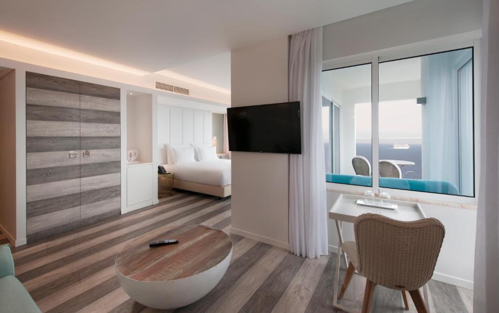 Mūsdienīgs viesnīcas numurs ar plašu logu, kurā redzams skats uz jūru, un elegantu interjeru ar koka grīdu un modernām mēbelēm. Numurā ir TV, galds un komfortabla atpūtas zona.