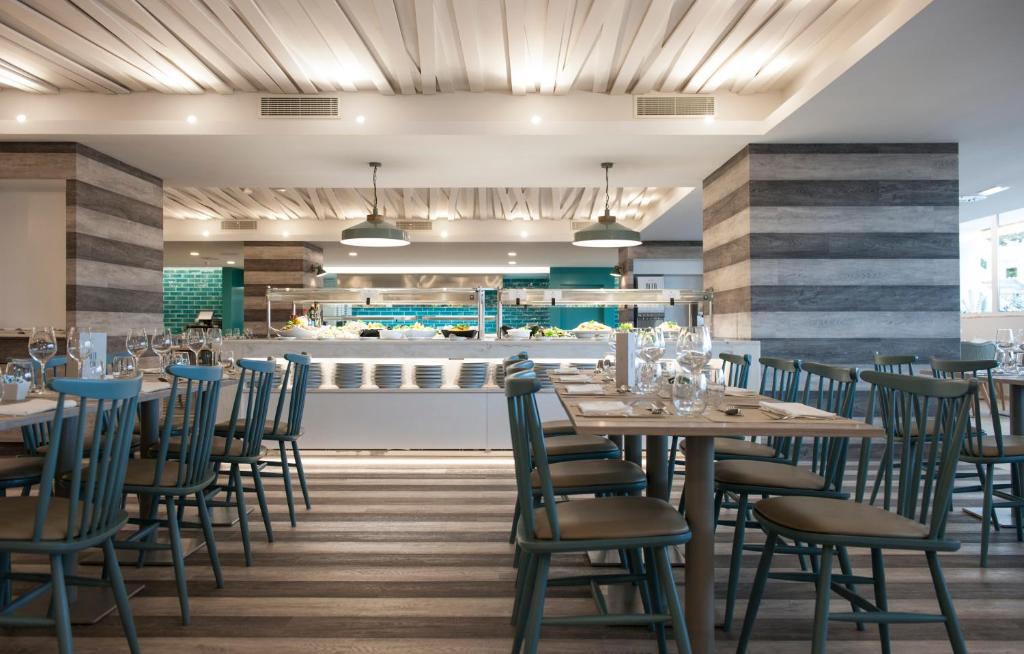 Mūsdienīgs restorāna interjers ar koka grīdu un stilīgām mēbelēm. Redzama atvērta virtuve un eleganti galdi ar galda piederumiem.