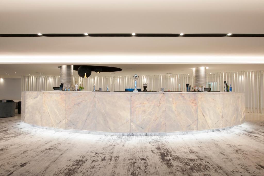 Mūsdienīgs viesnīcas reģistratūras dizains ar apgaismojumu un marmora virsmu. Telpa ir gaiša un eleganta, radot viesmīlīgu atmosfēru.