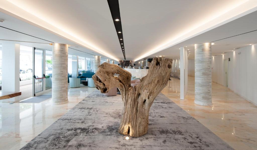 Mūsdienīgs viesnīcas vestibils ar lielu koka skulptūru centrā, apgaismots ar stilīgām gaismām un moderniem mēbeļu elementiem. Elegantā interjera dizainā apvienojas komforts un estētika.