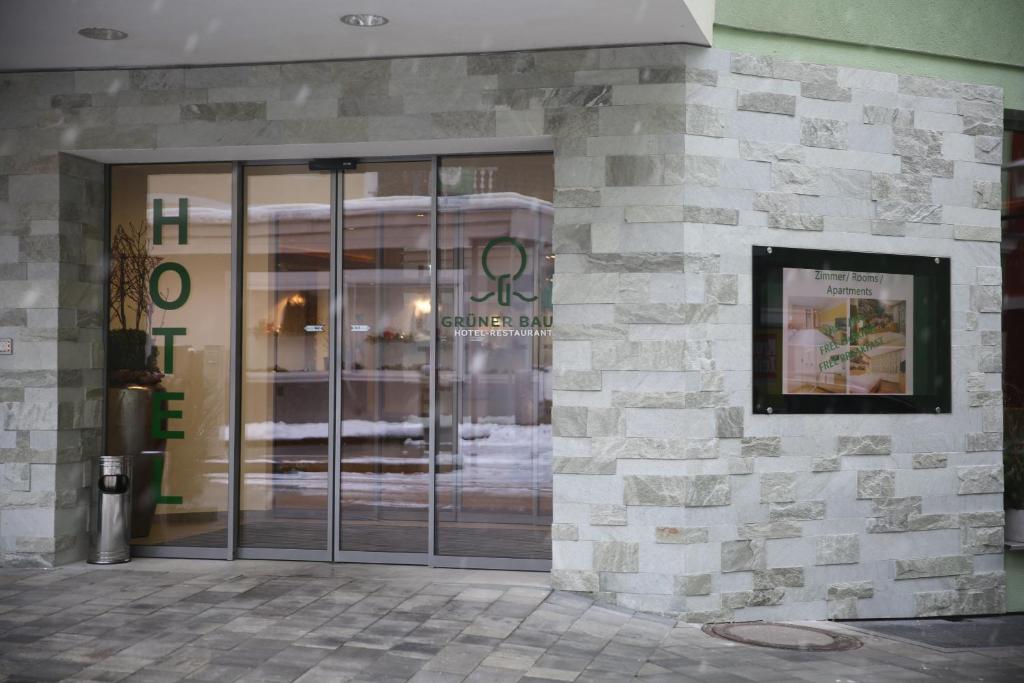 Ieejas durvis uz viesnīcu "Grüner Baum", ar mūsdienīgu akmens apdari un skaidri redzamu viesnīcas nosaukumu. Blakus redzama informācijas izkārtne par pieejamajiem numuriem un apartamentiem.