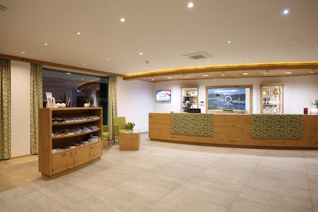 Mūsdienīgs viesnīcas reģistratūras interjers ar koka akcentiem, gaišām krāsām un komfortablu sēdvietu. Skats uz informācijas stendu un apkalpojošo personālu.