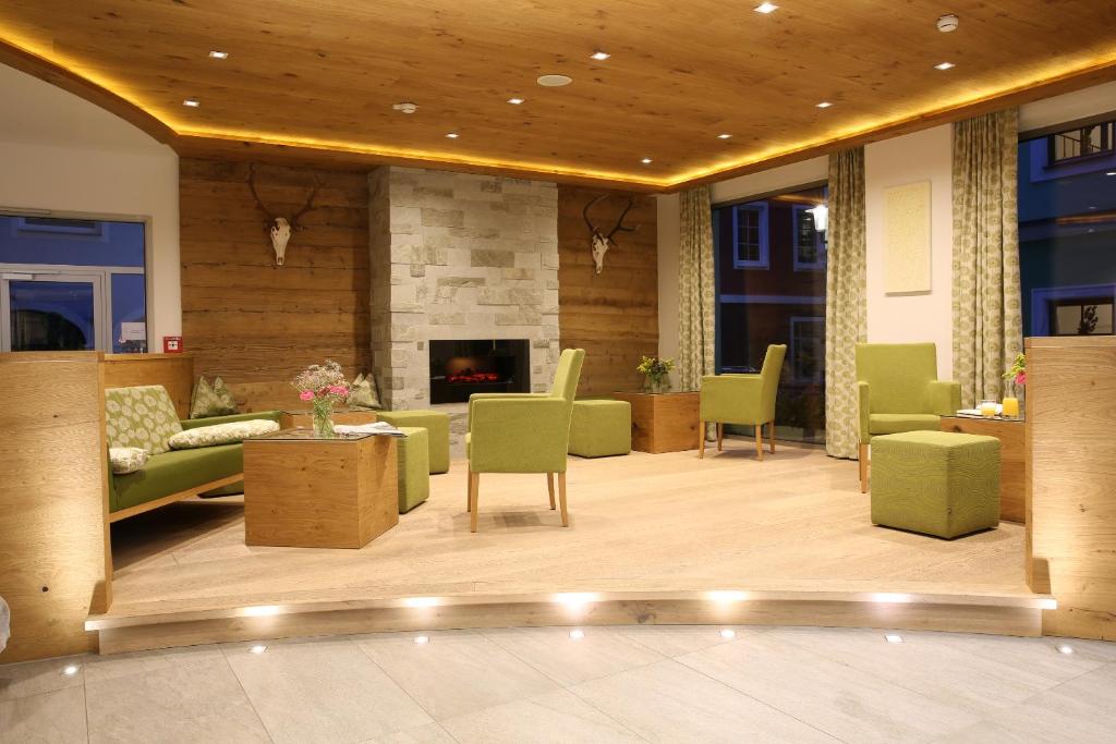 Mūsdienīgs un mājīgs viesnīcas interjers ar koka un akmens akcentiem, zaļiem mēbelēm un ērtām sēdvietām, kas rada relaksējošu atmosfēru.