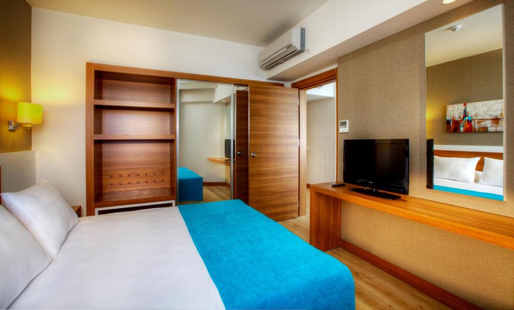 Mūsdienīgs viesnīcas numurs ar ērtu gultu, koka mēbelēm un televizoru. Interjers ir gaišs ar siltām krāsām un modernu dizainu.