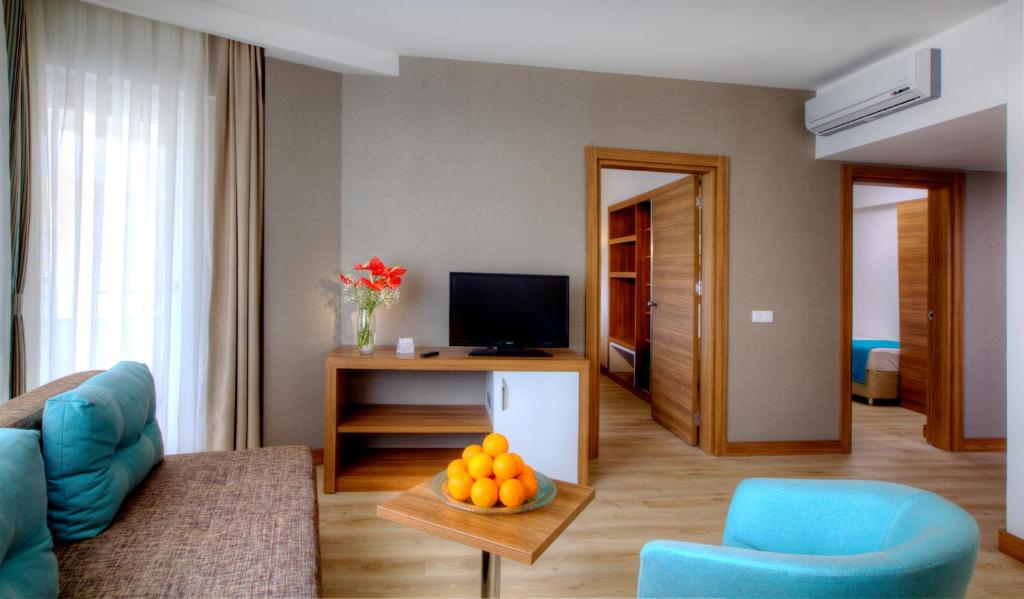 Mūsdienīgs viesnīcas numurs ar ērtu dīvānu, televizoru un dēlīšu galdu ar apelsīniem. Interjers ir gaišs un stilīgs, ar koka durvīm un logiem, kas ļauj ienākt dabiskai gaismai.