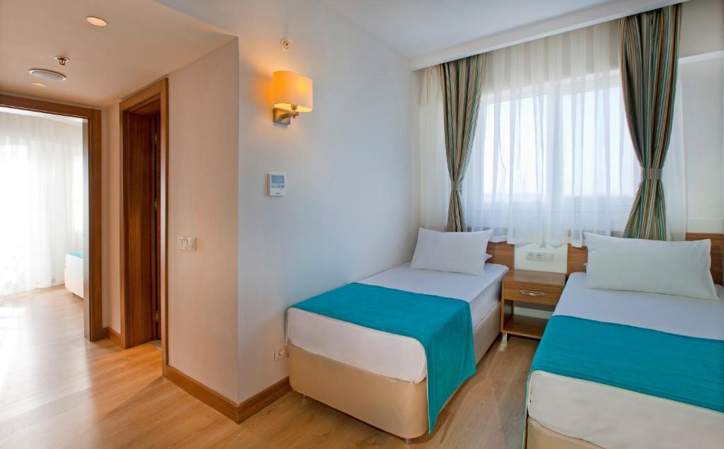 Gaiša viesnīcas istaba ar divām atsevišķām gultām, izrotāta ar zilu gultas pārklāju un lieliem logiem, caur kuriem ieplūst dabiska gaisma. Eleganta interjera dizains ar koka grīdu un mūsdienīgiem apgaismojuma risinājumiem.