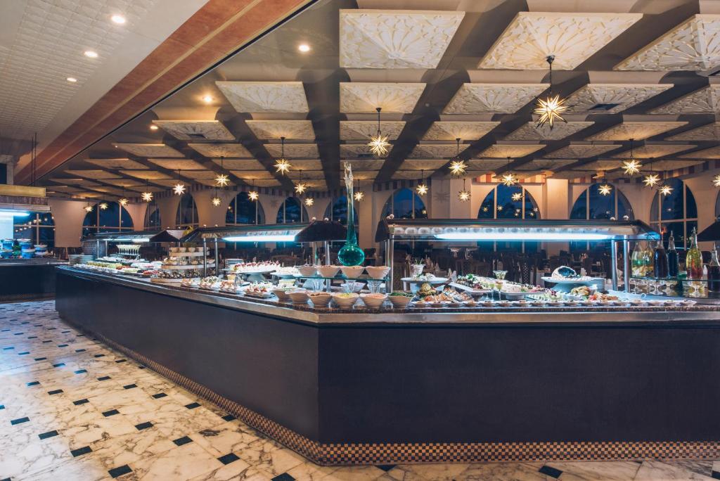 Elegants restorāns ar bufeti, kas piedāvā dažādus ēdienus, apgaismots ar modernām gaismām un dekoratīvām zvaigznēm. Interjers apvieno mūsdienīgu un klasisku stilu, radot patīkamu atmosfēru.