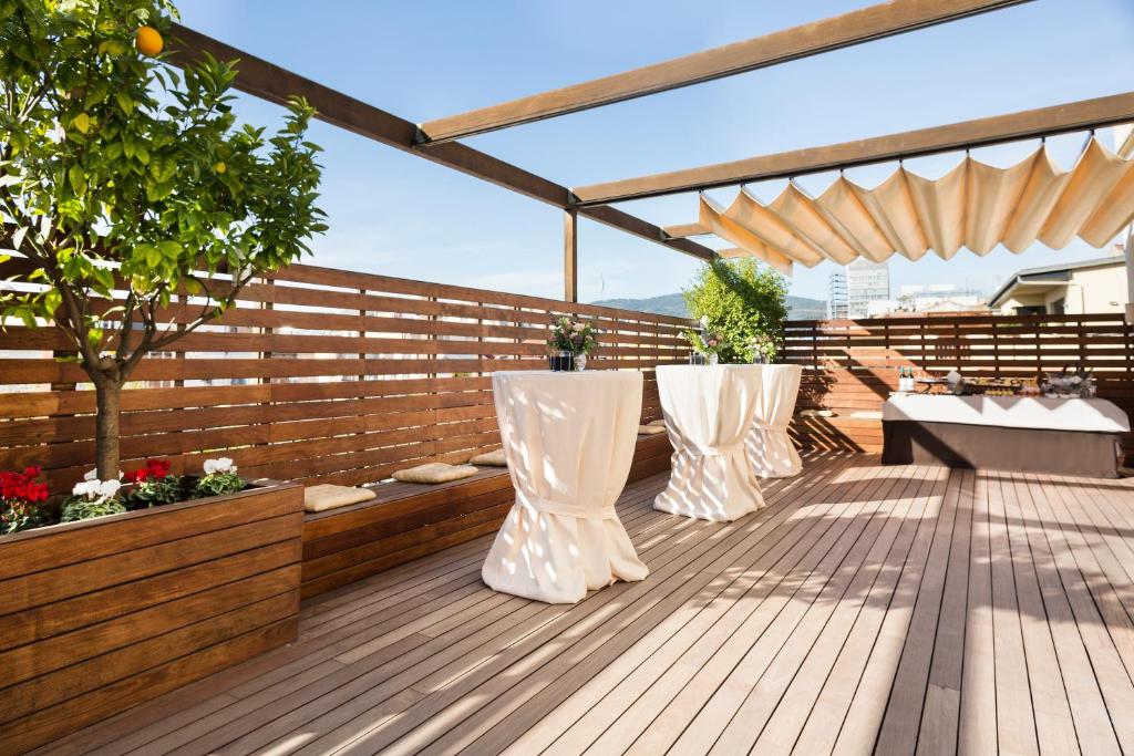 Terases vieta ar koka grīdu, dekoratīvām puķēm un galdiem ar baltām drānām, ideāla pasākumiem un atpūtai.