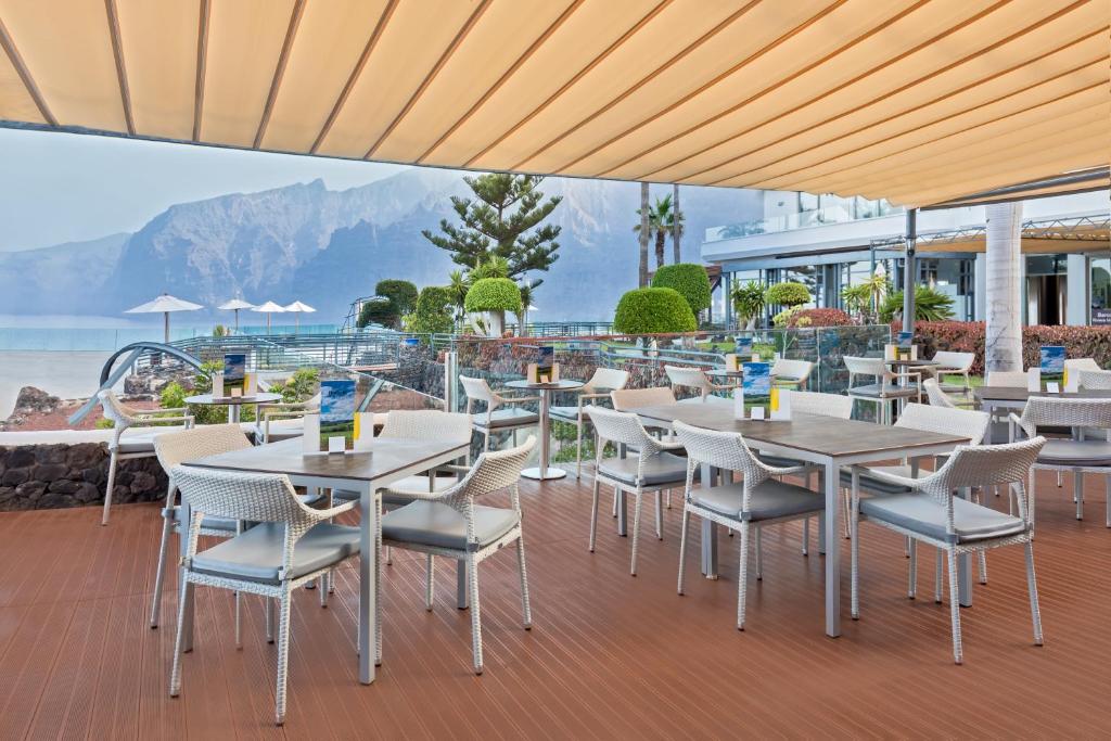 Āra restorāna zona ar baltiem galdiem un krēsliem, skats uz kalniem un jūru. Apzaļumotas vietas un sauļošanās krēslus papildina mierīga atmosfēra.