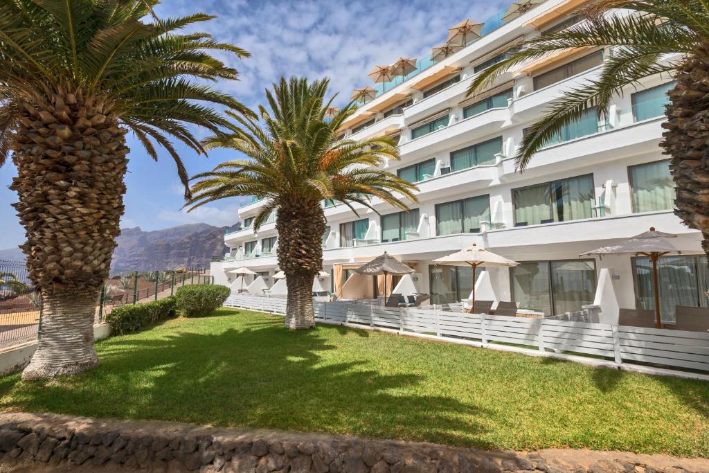 Viesnīca ar palmām un terasi, kas atrodas zaļā zālē, piedāvā relaksējošu atmosfēru un skaistus kalnu skatus. Ideāla vieta atpūtai un atjaunošanās brīvdienās.