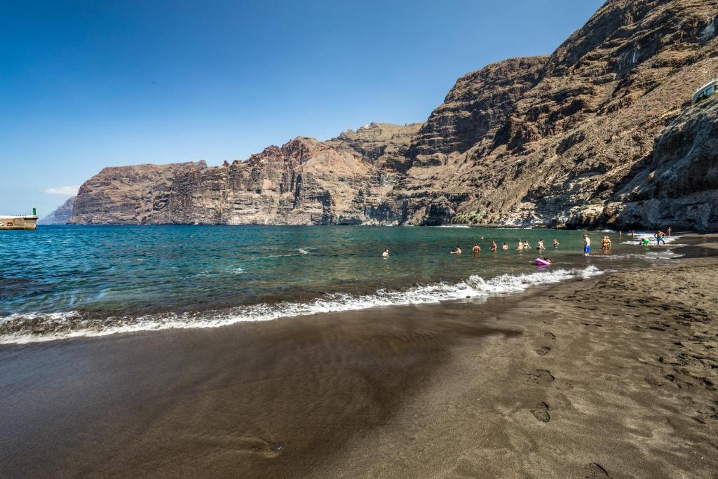 Skaista pludmale ar melnu smilšu un skaidru zilu ūdeni, ko ieskauj augstas klintis. Vairāki cilvēki bauda peldēšanu un saulēšanās prieku.