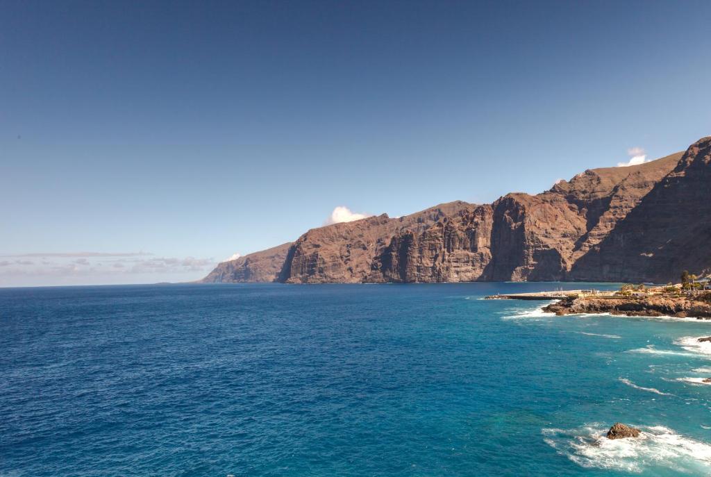 Krāšņa ainava ar klintīm un zilām jūrām, kas veido krāšņu piekrastes skatu. Saules gaisma izgaismo kalnus, radot mierīgu un dabīgu atmosfēru.