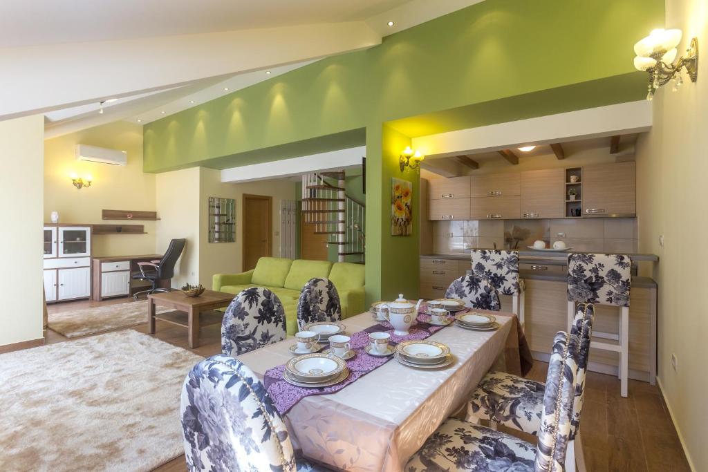 Mūsdienīga viesistaba ar atvērtu plānojumu un ēdamgaldu, kas dekorēts ar elegantām krēslu pārklājumiem. Gaiši zaļas un dzeltenas krāsas akcenti piešķir telpai siltumu un mājīgumu.