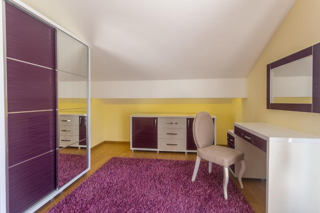 Mūsdienīgs un elegants guļamistabas interjers ar purpura krāsas akcentiem, iekļaujot spoguļskapju, galdu un krēslu uz mīksta paklāja. Sienas ir gaiši dzeltenas, radot siltu atmosfēru.