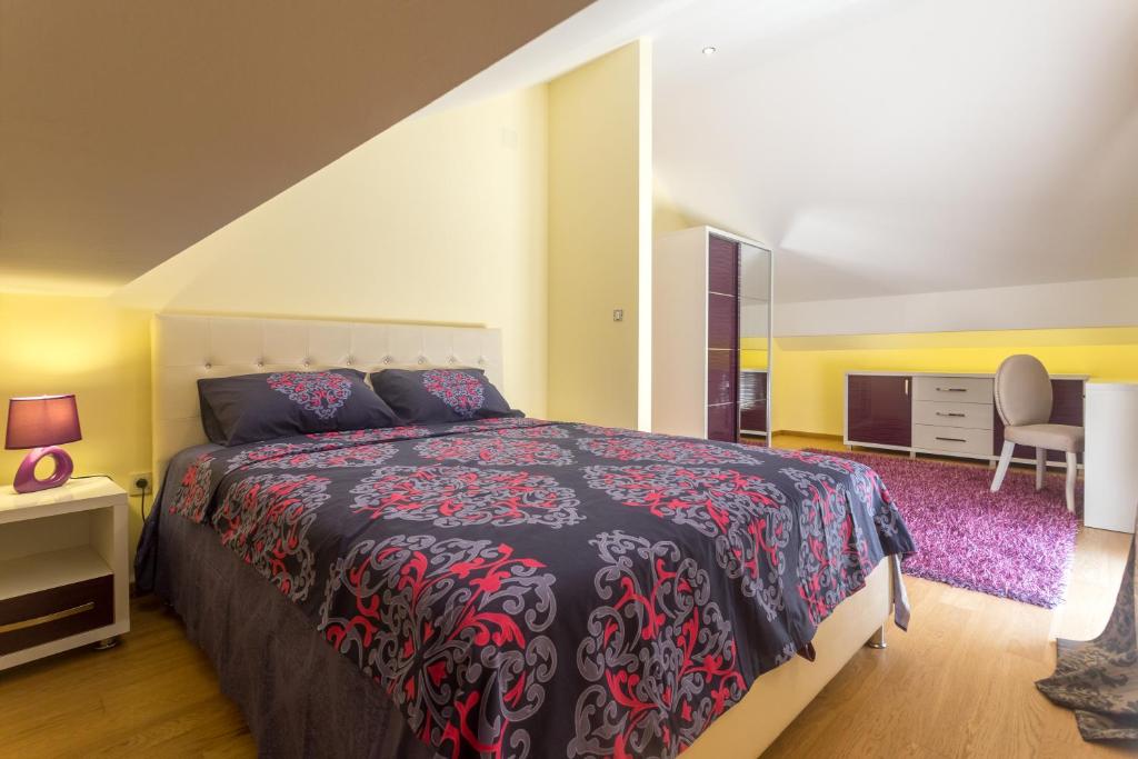 Mūsdienīga guļamistaba ar divguļamo gultu, dekoratīvu gultas veļu un elegantu rakstāmgaldu. Telpā ir gaišas krāsas un mīksts paklājs, radot mājīgu atmosfēru.