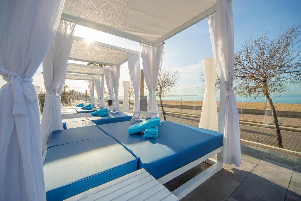 Mūsdienīgs atpūtas zona pie pludmales ar zilām gultām un baltiem aizkariem, kas nodrošina komfortu un relaksāciju. Skaista jūras ainava un saulaina atmosfēra.