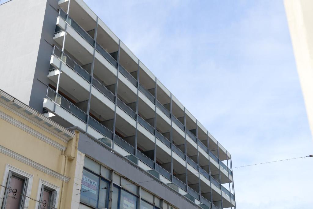 Moderns daudzstāvu ēka ar balkoniem un stikla margām, kas atrodas blakus citai vēsturiskai ēkai. Sky ir skaidrs un gaišs.