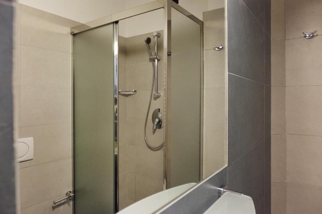 Mūsdienīga duša ar stikla durvīm, apkārtējās flīzes ir gaišas un neitrālas krāsas, radot svaigu un tīru izskatu.