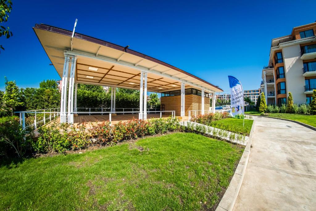 Moderns paviljons ar zaļo zāli un apstādījumiem, blakus ēkai un ziliem debesīm. Ideāla vieta atpūtai un pasākumiem.