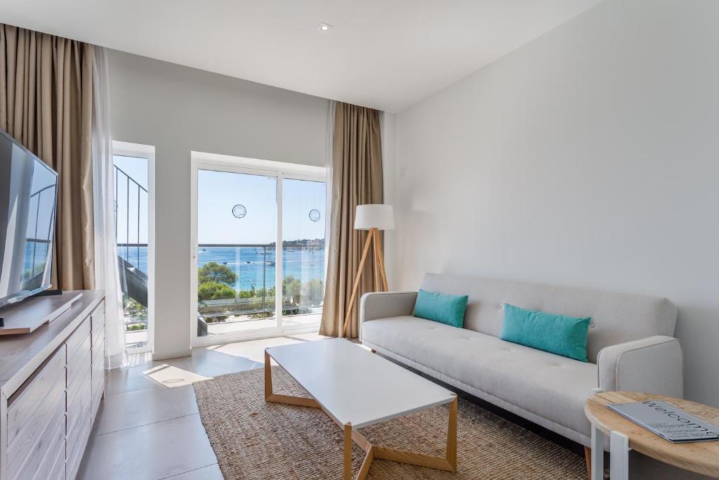 Mūsdienīgs viesistabas interjers ar skatu uz jūru, kurā ir gaišas krāsas dīvāns un stikla durvis, kas ved uz āra terasi.