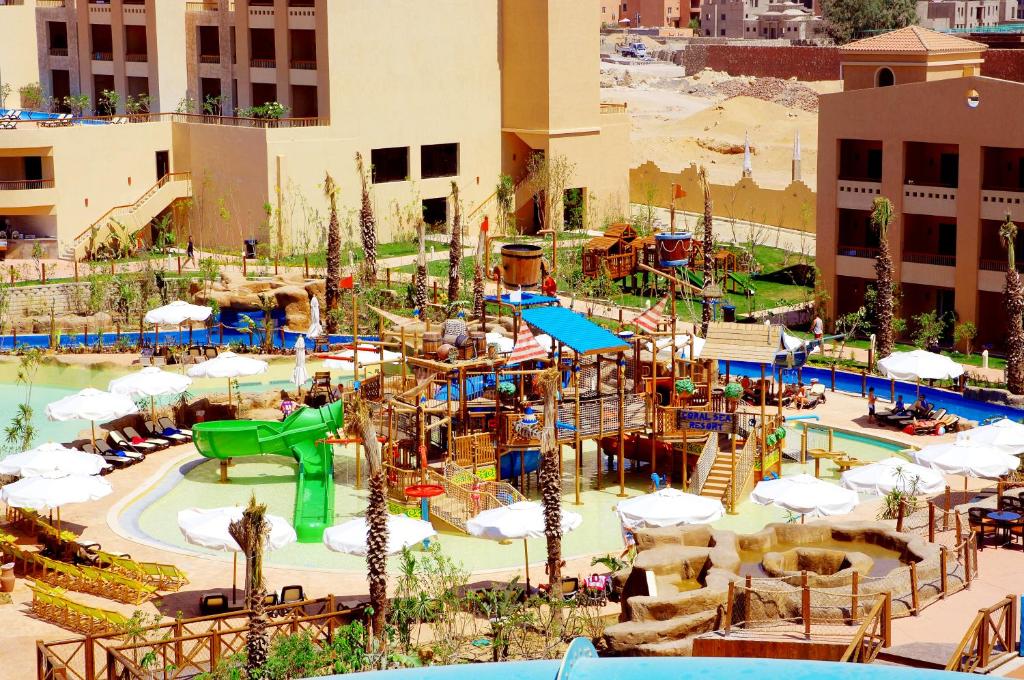 Ūdens atrakciju parks ar slidkalniņiem un peldbaseiniem, apņemts ar saulessargiem un atpūtas krēsliem. Apkārtne ir zaļa ar palmām un viesnīcas ēkām.