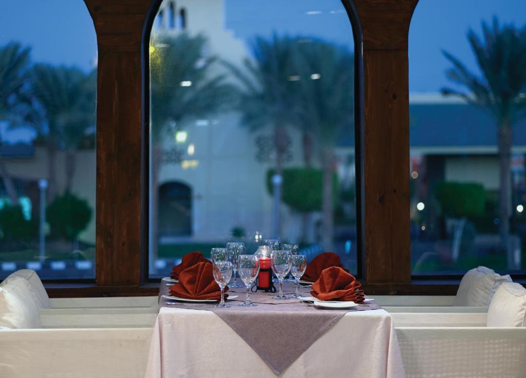 Elegants restorāns ar galdu, kas klāts ar glāzēm un sarkaniem salvetēm, logā redzams zaļojošs ainava un zema apgaismojuma noskaņa.