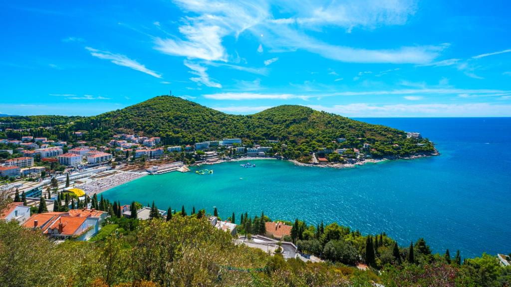 Skaista piejūras ainava ar zaļām kalnu virsotnēm, zilu ūdeni un pludmali, kas ir ideāla atpūtai.