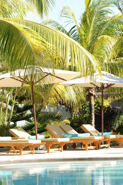 Saulainā atpūtas zona ar pludmales krēsliem, saulessargiem un tropiskām palmām ap peldbaseinu. Ideāla vieta relaksācijai un atpūtai.
