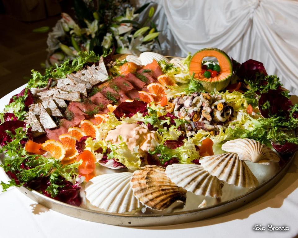 Skaisti noformēts uzkodu šķīvis ar dažādām delikatesēm, tostarp gaļu, jūras veltēm un dārzeņiem, dekorēts ar augļiem un zaļumiem. Ideāli piemērots svinībām vai svētku mielastiem.
