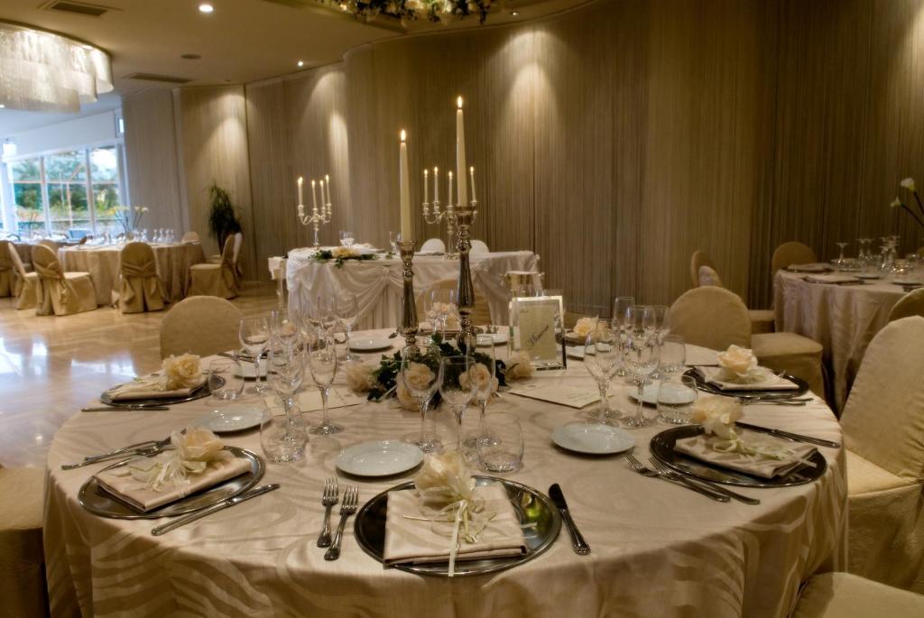 Elegants galda iestatījums svinīgai pasākumam ar baltiem ziediem un sveču turētājiem. Moderns interjers ar mīkstām krēsliem un romantisku apgaismojumu.