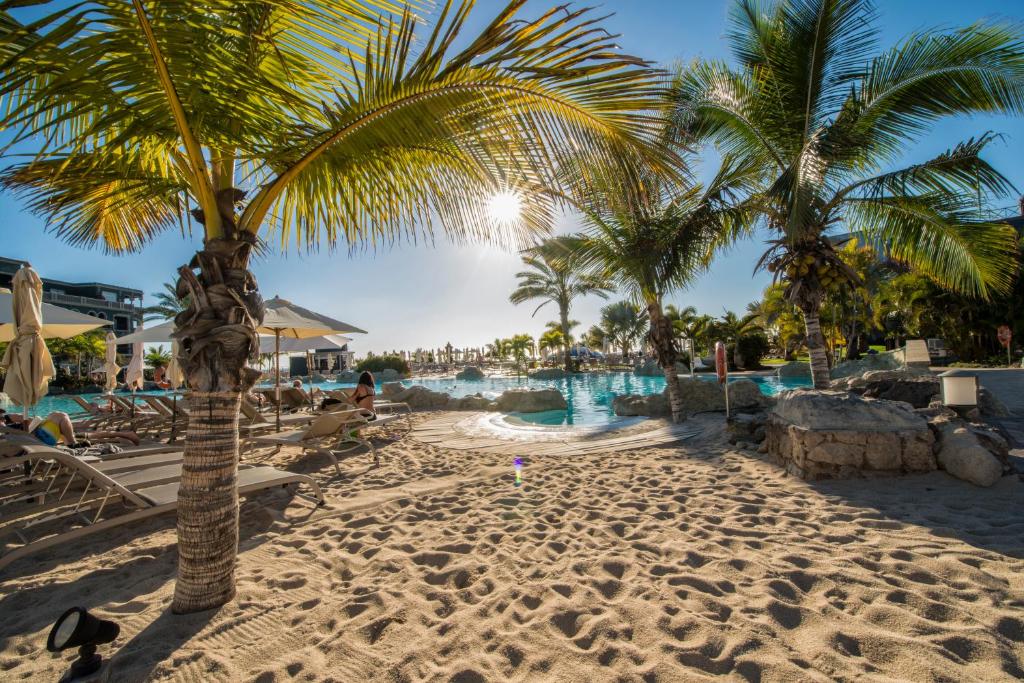 Tropu pludmale ar palmām, sauli un baseinu, kas aicina uz atpūtu. Smilšu pludmale un sauļošanās krēsli nodrošina relaksējošu atmosfēru.