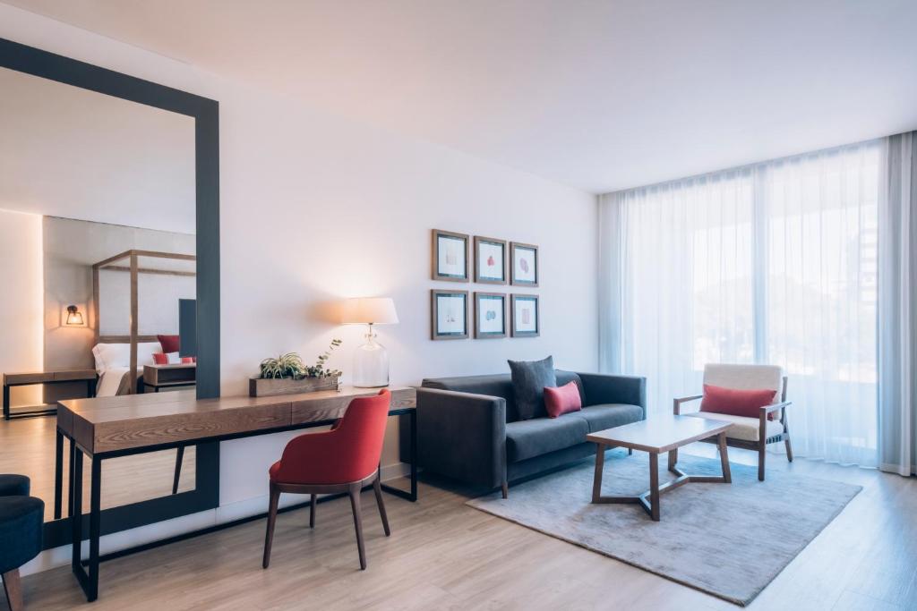 Mūsdienīga viesnīcas istaba ar elegantu dizainu, kurā ir dīvāns, galds un krēsli. Lielie logi nodrošina daudz gaismas, radot patīkamu atmosfēru.