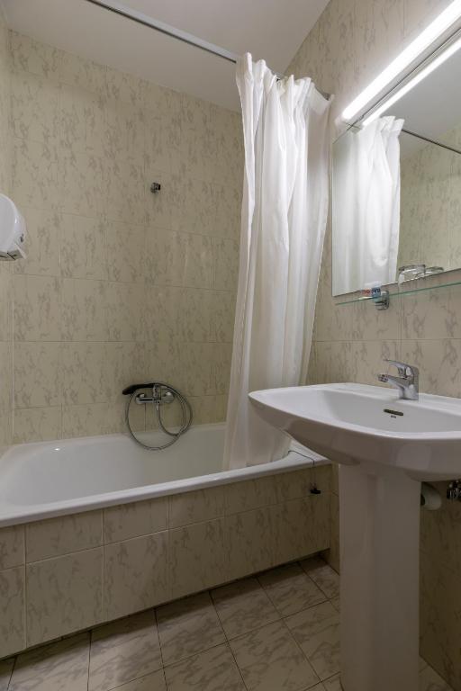 Vannas istaba ar baltu vannu, izlietni un dušas aizkaru, ar neitrālām krāsām un mūsdienīgu dizainu.