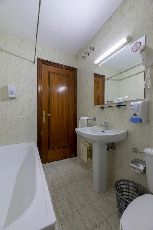 Mūsdienīgs vannas istabas interjers ar vannu, izlietni un spoguli, kas nodrošina funkcionalitāti un ērtību. Gaismas avots un higiēnas piederumi piešķir telpai patīkamu atmosfēru.