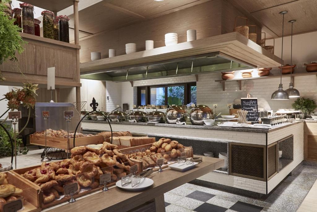 Mūsdienīga bufete ar dažādiem ēdieniem, tostarp konditorejas izstrādājumiem un siltajiem ēdieniem, iekārtota eleganti ar dabīgiem elementiem un modernu dizainu.