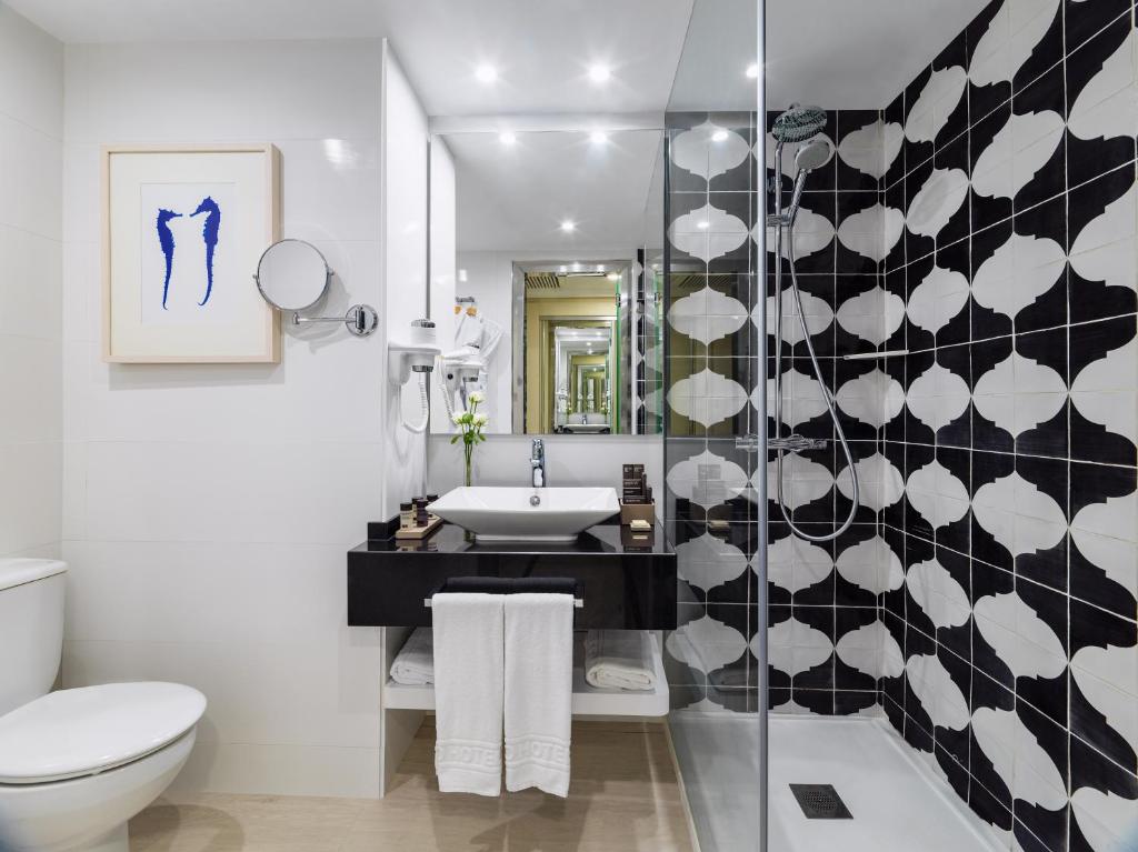 Moderns vannas istabas interjers ar melnbaltām flīzēm, stilīgu izlietni un mākslas darbu uz sienas. Svaigi ziedi un mūsdienīgas iekārtas piešķir telpai eleganci.