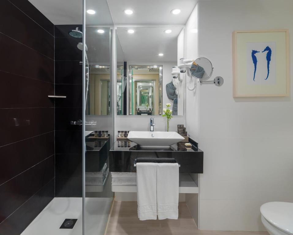 Mūsdienīgs vannas istabas interjers ar melnu flīžu sienām, stikla dušu un elegantu izlietni, papildināts ar dekoratīvu zīmējumu un ziedu kompozīciju.