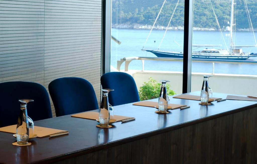 Konferenču telpa ar skatu uz jūru, kur uz galda novietoti stikla ūdens karafes un piezīmju bloki. Mūsdienīgs interjers ar zilām krēslām un lieliem logiem, kas nodrošina dabīgu apgaismojumu.