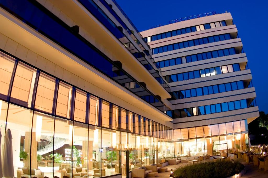 Mūsdienīga viesnīca ar plašiem stikla logiem, kas izgaismoti naktī, radot siltu un viesmīlīgu atmosfēru. Apburošs arhitektūras dizains ar terasi.