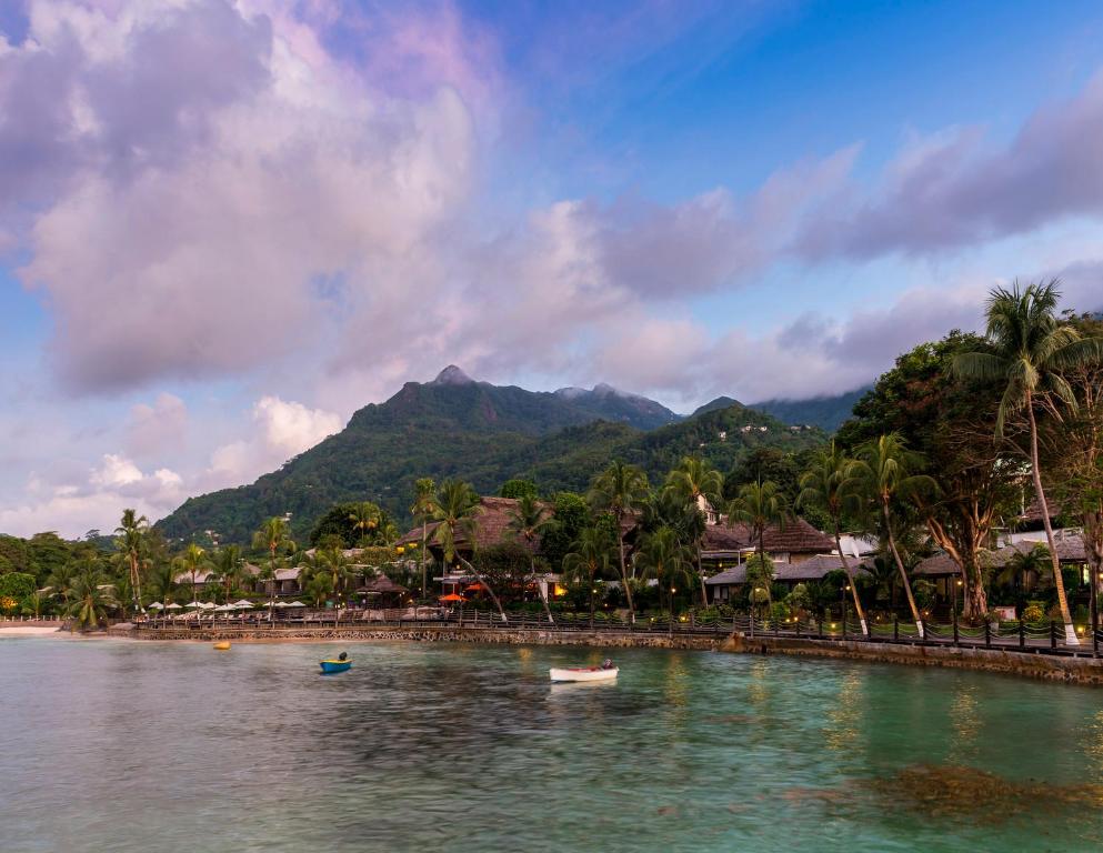 Tropu pludmale ar palmām un kalnu fonā, kas atspoguļojas mierīgā ūdenī. Apkārt esošās viesnīcas un restorāni rada relaksējošu un idillisku atmosfēru.