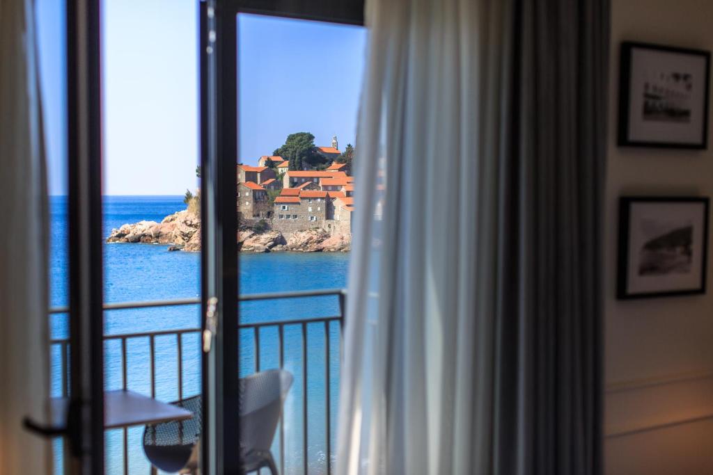 Skats no viesnīcas loga uz jūru un gleznainu salas ainavu ar mājām ar sarkaniem jumtiem.